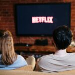 Netflix rachète Warner Bros : Vers une nouvelle ère… et une hausse des prix en 2026 ? A couple enjoys a relaxed evening watching Netflix in their living room.
