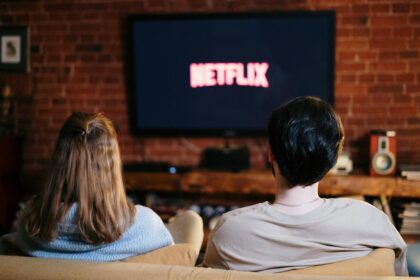 Netflix rachète Warner Bros : Vers une nouvelle ère… et une hausse des prix en 2026 ? A couple enjoys a relaxed evening watching Netflix in their living room.