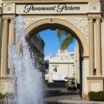 View of the iconic Paramount Pictures archway and fountain on a sunny day in Hollywood, California.