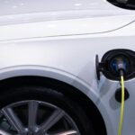 2026 : TESLA VS BYD A white electric car is plugged in for charging, close-up view of the charging port.